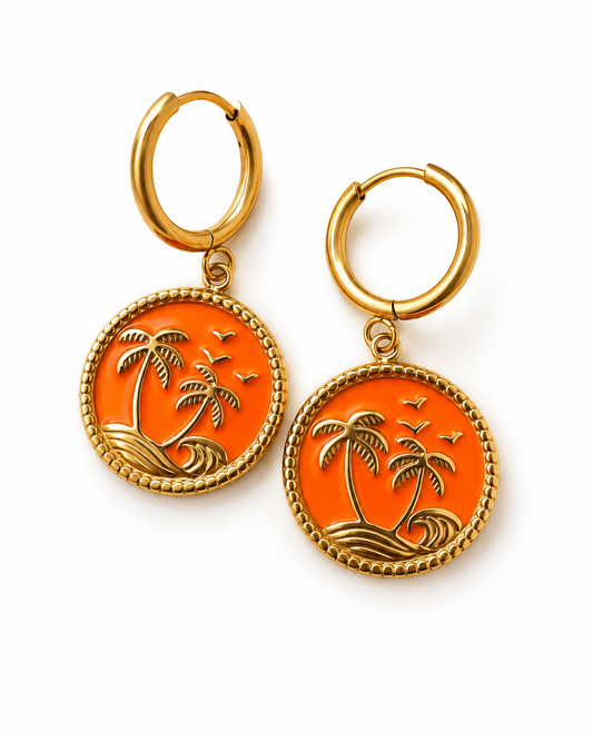 A pair of gold hoop earrings with round orange enamel pendants featuring an engraved tropical palm tree and wave design, shown on a clean white background.