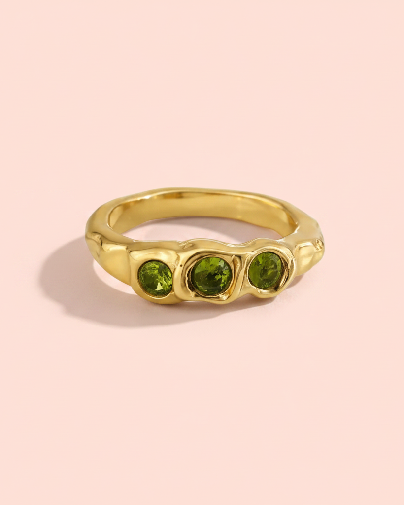 Gold ring with three green gemstones on a white background
