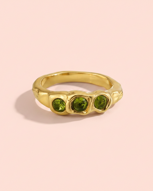 Gold ring with three green gemstones on a white background