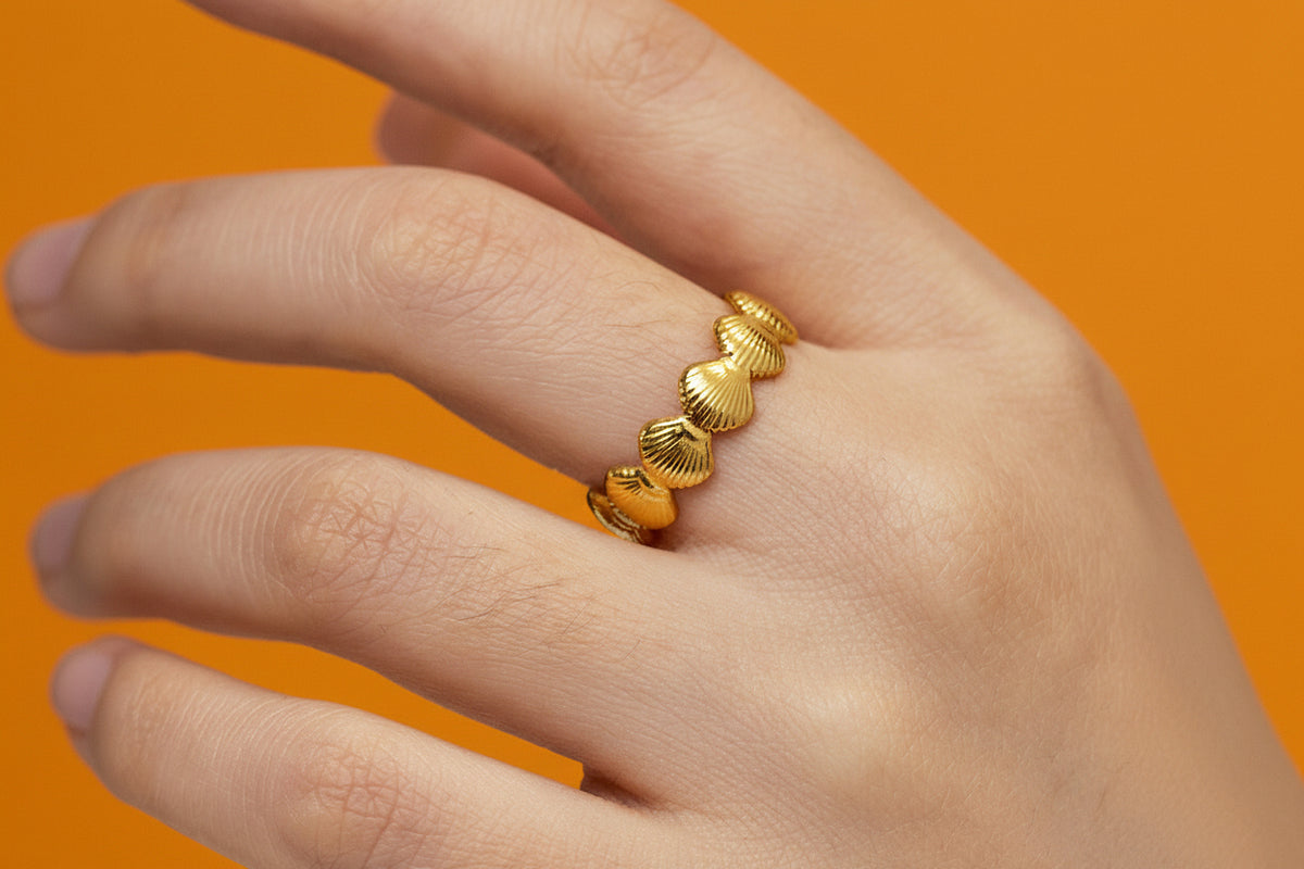 Gold ring with shell design on a hand against a gray background