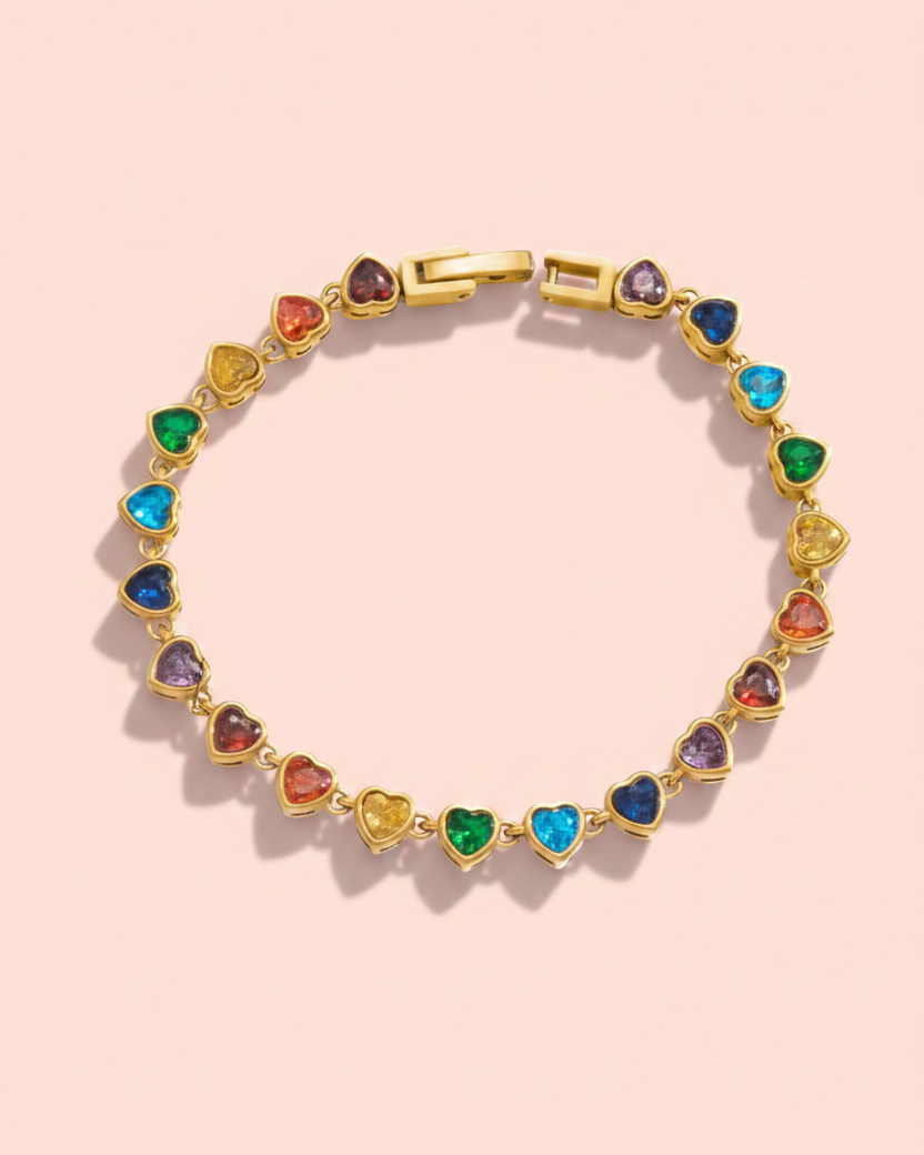 A gold-plated heart-link bracelet with colorful heart-shaped gemstones in multiple colors, displayed on a soft pink background.