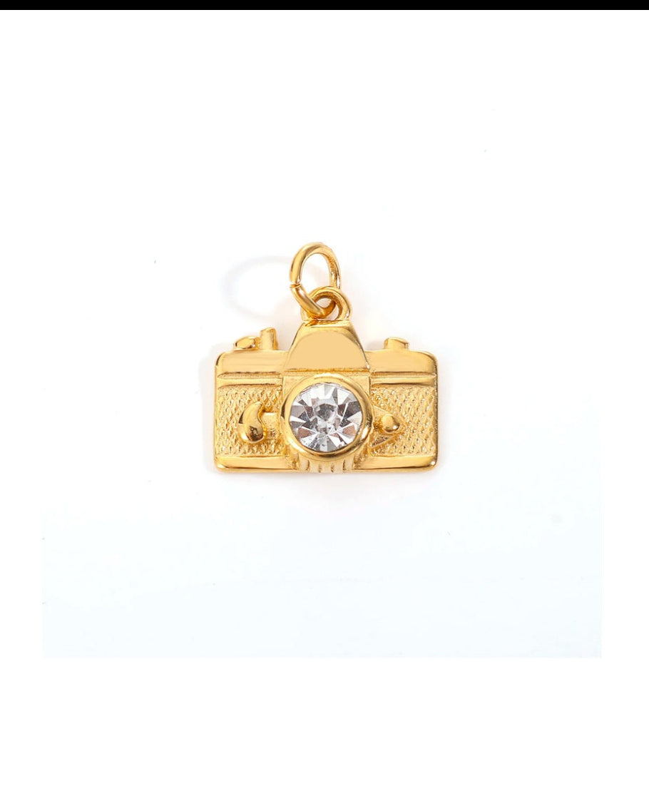 Gold camera-shaped charm with a clear gemstone on a white background